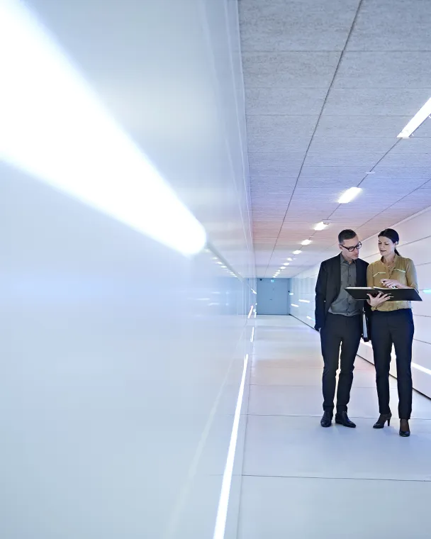 Two colleagues walk down an office hallway while conversing