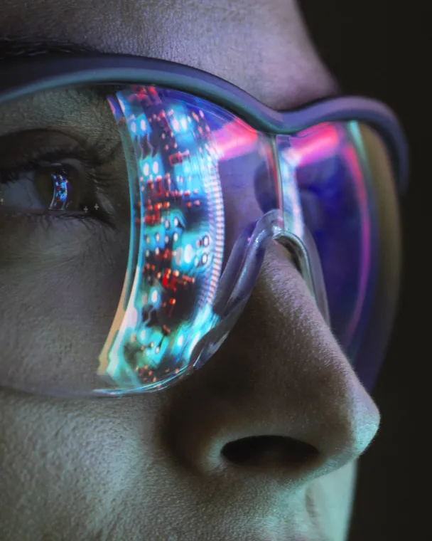 close up of a woman's face wearing safety glasses, with a computer screen shown in the reflection