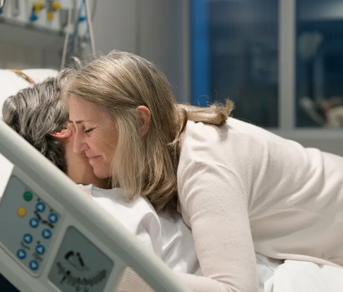 Woman hugs a patient in a hospital bed
