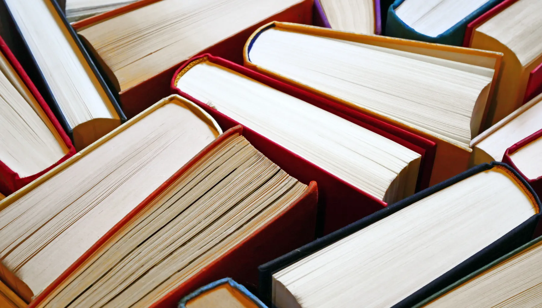 The tops of many hard cover books, showing the pages and spine standing up in an irregular pattern