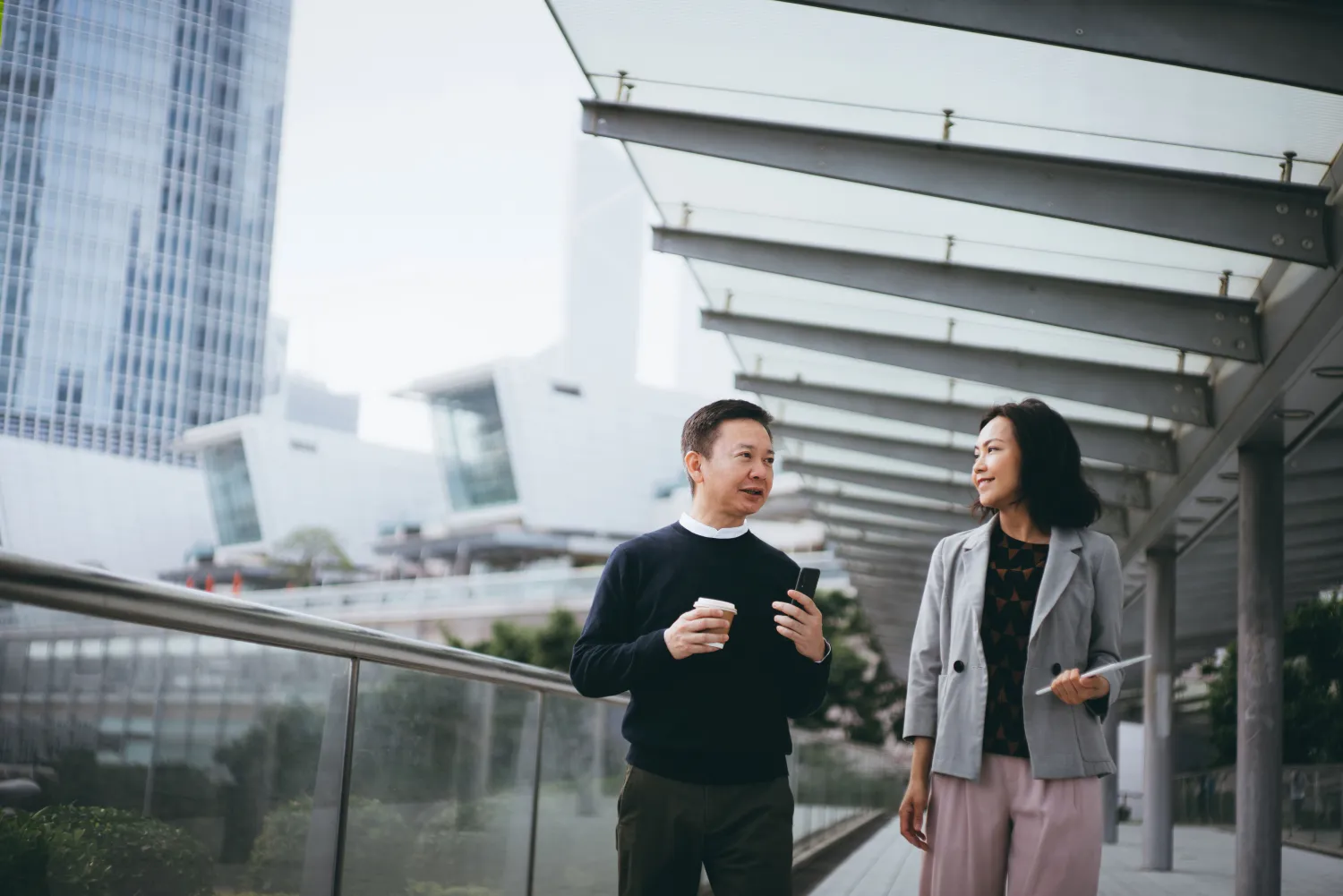 Two colleagues walk and talk on an exterior, elevated walkway